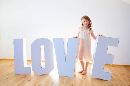 Girl 7 years old playing with big cardboard 3D Standing Letters forming word LOVE from white cardboard on a light background. Relationship concept.の写真素材
