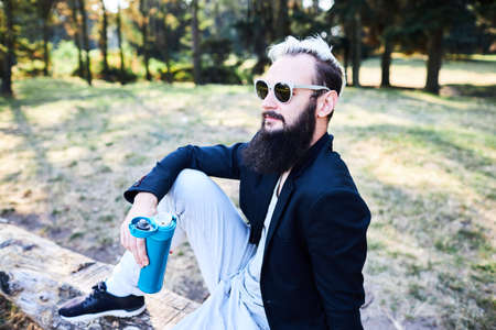 Portrait of handsome bearded man drinking hot tea outdoor in trip on foot. Strong and brave man with beard have a rest on hiking trail. Time for relax.の写真素材