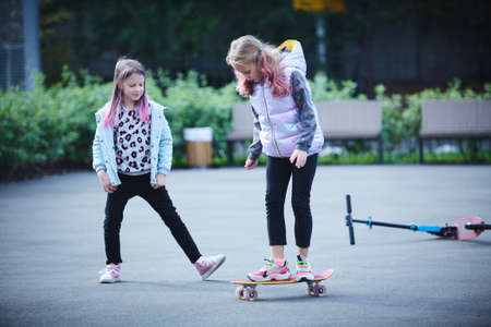 Two pretty little sisters having fun together learning to skateboard outdoors. The concept of a healthy lifestyle. Kids sportの写真素材