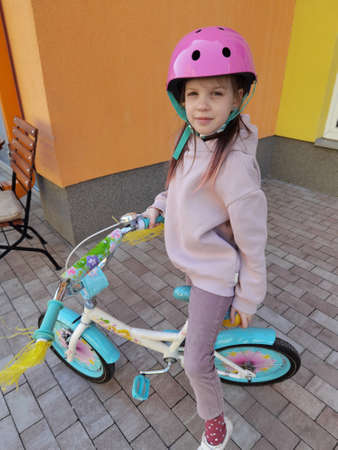 Portrait of a playful funny girl in a pink safety helmet on her bikeの写真素材