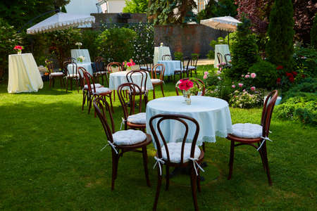 Round table covered with white cloth and chairs stand on a green lawn outdoors.の写真素材