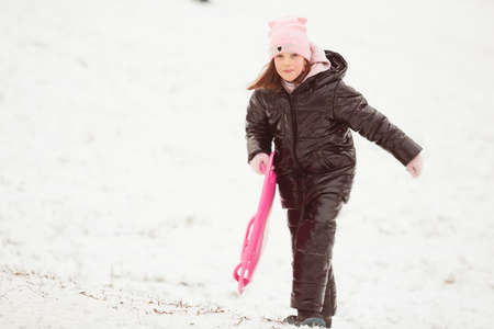 Happy little girl sliding down the hill on saucer sled. Girl enjoying slider ride on the snowの写真素材