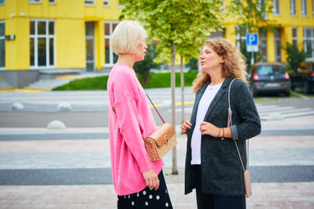 Two women friends laughing and hugging outdoors.の写真素材