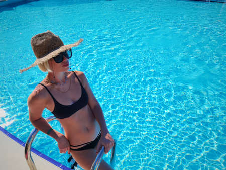 Sexy Woman in Swimsuit is Relaxing in Swimming Pool. Beautiful Woman Wearing Straw Hat and Relax Sunbathe in Poolside on Summer Holiday at Resort Hotel, Leisure Activities and Relaxation Timeの写真素材