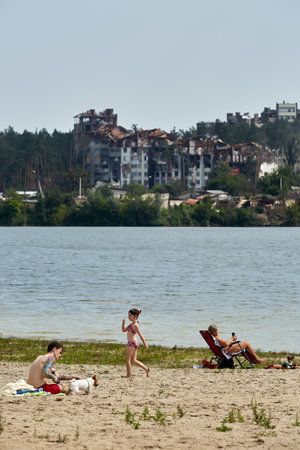 Irpin, Kyiv region, Ukraine - 25 August, 2022: Citi after the Russian occupation. People are having rest near lake opposite destroyed houses.のeditorial素材