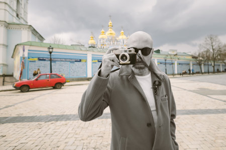 Handsome beard photographer makes pictures on film retro camera in the Kyiv city, Ukraine.
