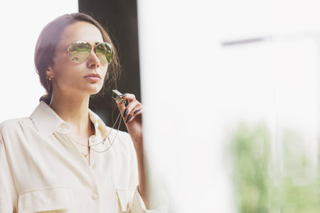 Portrait of attractive brunette holding whistle in her hand. Fashionable young woman with long hair in white costume standing in interior. Fan, coach, counselor.の写真素材