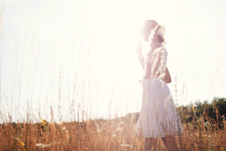 Portrait of young woman walking among high grasses in summer meadow wearing straw hat and linen dress enjoying nature. Harmony and balanceの写真素材