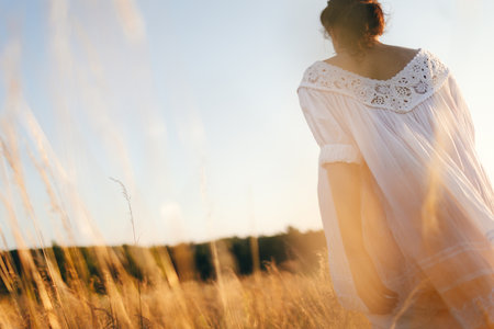 Brunette young woman in wild field. Natural beauty and romance concept. Sunset light. View from the back.の写真素材