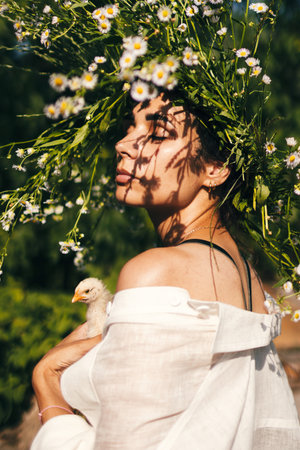 A beautiful young shuman in a wreath of daisies on her head and holds chick in her handsの写真素材