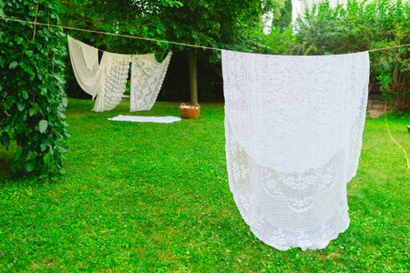 White laundry on clothesline in garden. White curtains drying in the sun.