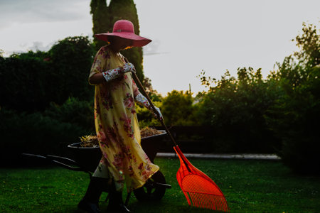 A woman dressed in a floral summer dress and wide-brimmed sun hat is seen tending to a garden during...