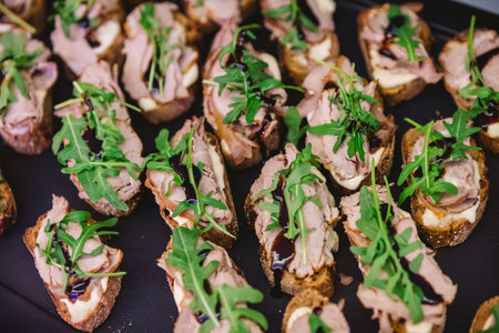 A tray of gourmet bruschetta appetizers featuring slices of bread topped with meat, arugula, and a drizzle of balsamic glaze, perfect for parties or gatherings.の写真素材