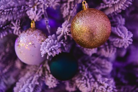 A close-up of a Christmas tree adorned with glittery ornaments. The image features a gold glitter ball, a white ornament with gold specks, and a dark green bauble, all hanging on frosted branches.の写真素材