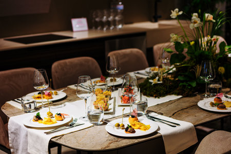 Luxurious dining table setup featuring gourmet appetizers, elegant glassware, floral centerpiece, and sophisticated decor, ideal for upscale events, weddings, banquets, and exclusive dinner parties.の写真素材