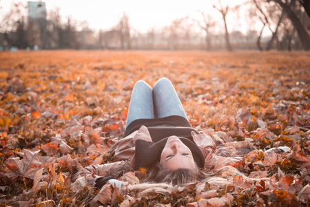 Girl lying on the autumn leaves in to the sunの写真素材
