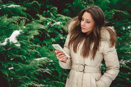 Girl in green snowy forest looking at mobile phone seriouslyの写真素材