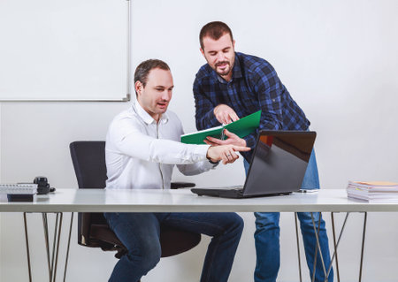Two men discussing and pointing at computer and note bookの写真素材