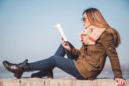 Girl reading while sitting on a wallの写真素材