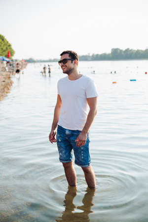Handsome man smiling and standing in the water wearing sunglassesの写真素材