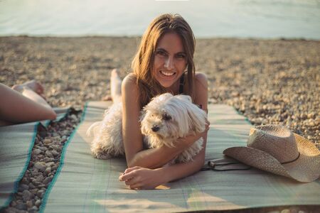 Girl with dog lying on the beach and smiling. Sunsetの写真素材