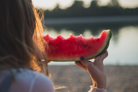 Girl eating watermelon and looking at the water. Sunsetの写真素材