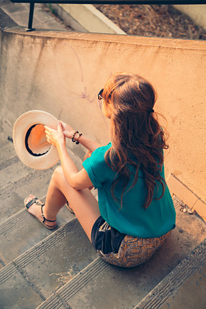 Girl sitting on the stairs and holding her hatの写真素材