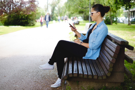 Girl sitting on the park bench and looking at the phoneの写真素材