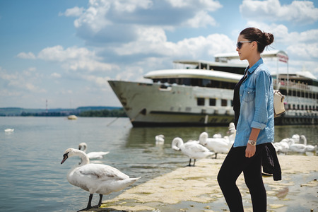 Girl looking at the river with swans on the shore. Sunny dayの写真素材