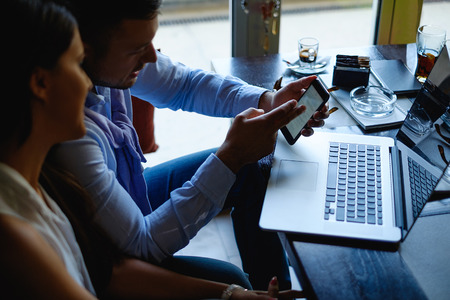 Businessman showing phone to his female colleague by the windowの写真素材
