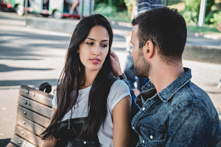 Couple sitting on a park bench looking at each other on a suuny dayの写真素材