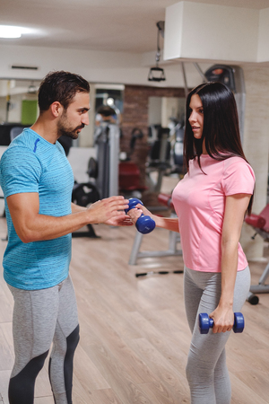 Male trainer seriously train girl biceps with dumbbells. Gym indoorsの写真素材