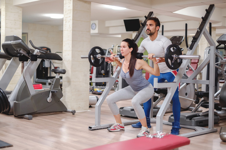 Girl doing squats with trainer in the gymの写真素材