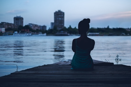 Girl alone looking at the city by the water from the pierの写真素材