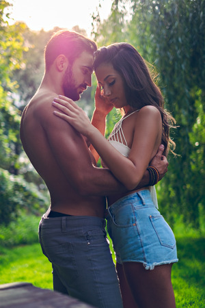 Couple hugging and caressing in the park with sun behind themの写真素材