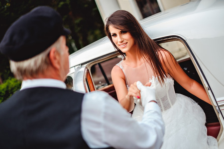 Driver helping bride to get out of the car while she is smilingの写真素材