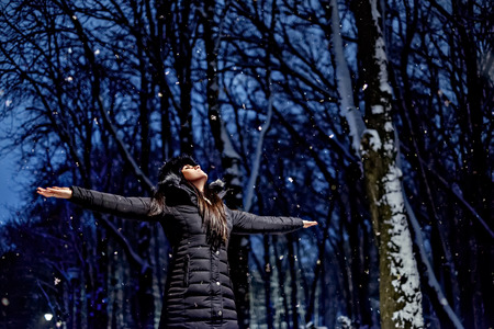 Woman lifting hands up and catching snowflakes in the park with her eyes closedの写真素材