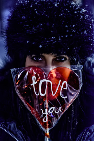 Girl holding lollipop with sign "Love you" on a snowy eveningの写真素材