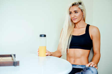 Healthy blonde fit woman in sportswear sitting on chair drinking juiceの写真素材