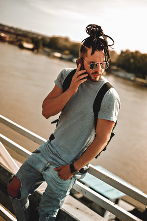 Man with dreadlocks and beard talking angry on the phone by the river on a hot summer dayの写真素材