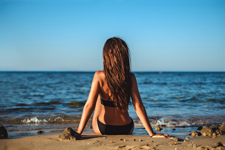 Young woman sitting on the tropical beach and watching the seaの写真素材