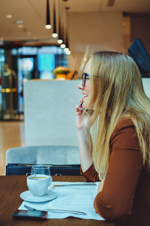 Woman talking on the phone and smiling in the restaurant. Coffee and water are on the tableの写真素材