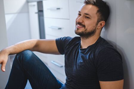 Handsome bearded man sitting on the kitchen floor and smilingの写真素材