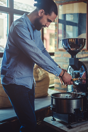 Hipster man pouring coffee beans which he roasted in a retro roasterの写真素材