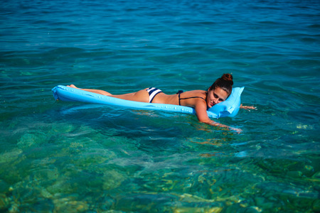 Girl smiling while resting and tanning on a floating bedの写真素材