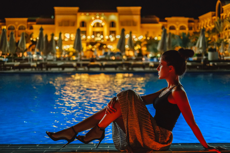 Girl in a dress sitting on the pool edge in the eveningの写真素材