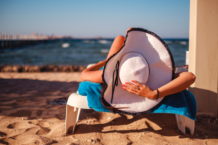 Girl holding hat while lying on the beach and tanningの写真素材