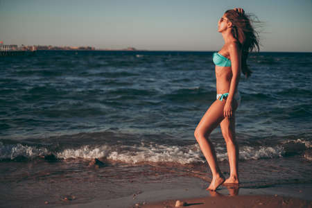Girl standing on the windy beach in sunset while holding hairの写真素材