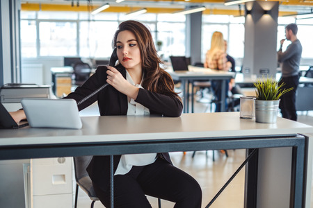 Serious business woman using phone in the office with colleagues in the backgroundの写真素材