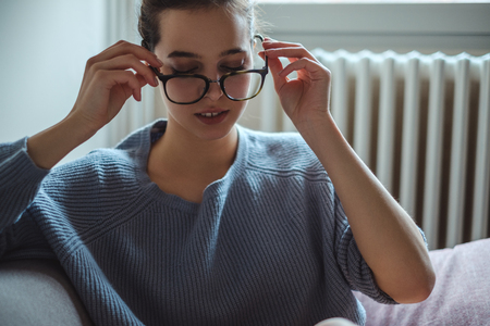 Beautiful girl putting on glasses in the roomの写真素材
